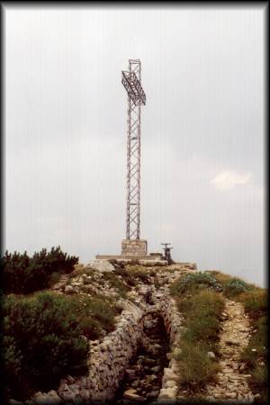 Das riesige eiserne Gipfelkreuz am Monte Maggio mit altem Schützengraben in Front